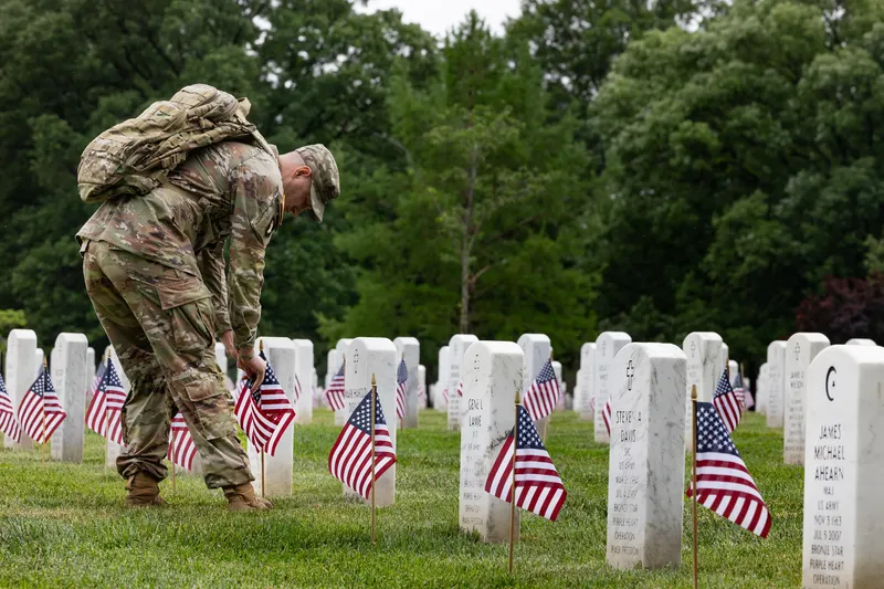 A soldier of the Old Guard placing small American flags at white headstones during 'Flags In' at Arlington National Cemetery for Memorial Day, near Washington, D.C.