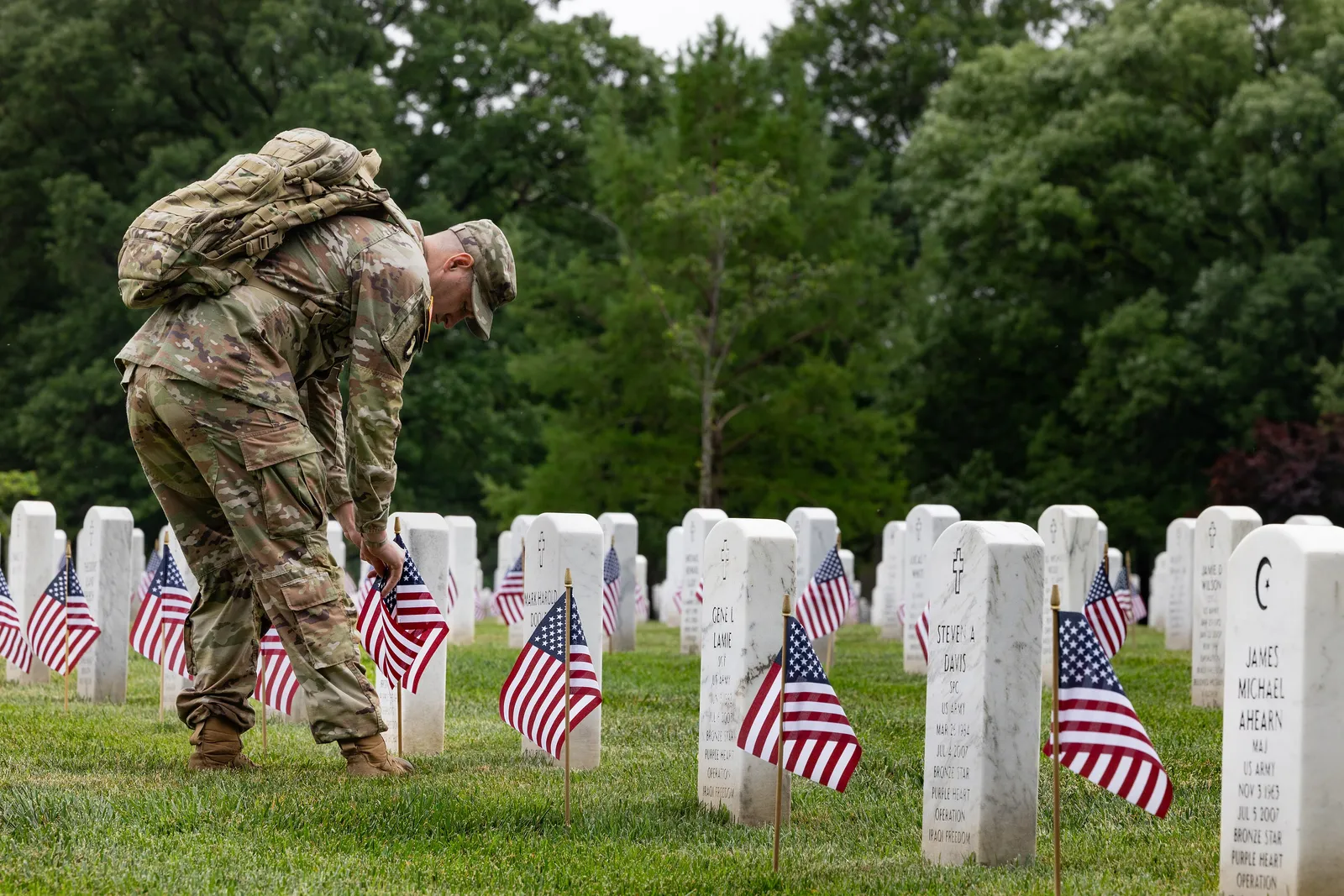 A soldier of the Old Guard placing small American flags at white headstones during 'Flags In' at Arlington National Cemetery for Memorial Day, near Washington, D.C.