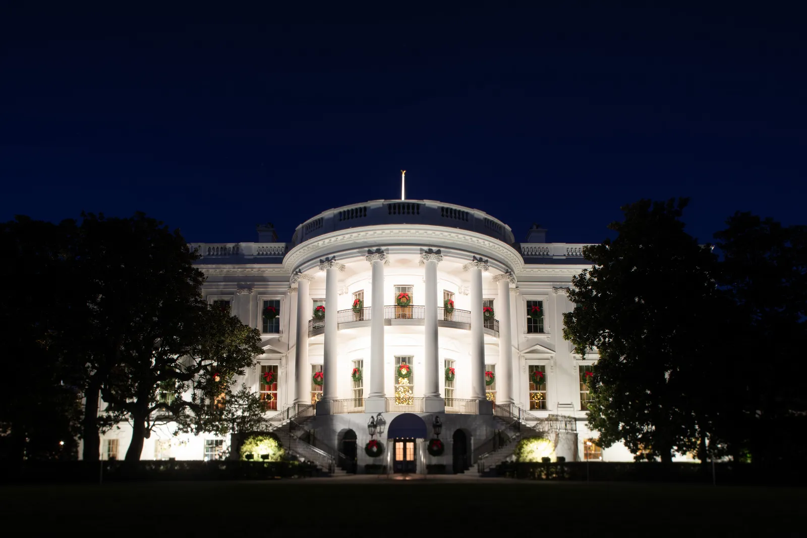 The floodlit White House at dusk with Christmas wreaths in every window and on the door, dressed for the holidays, in Washington, D.C.